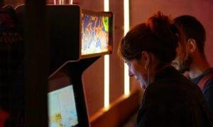 Henkilö pelaa videopeliä arkadipelikoneessa valaistussa ympäristössä