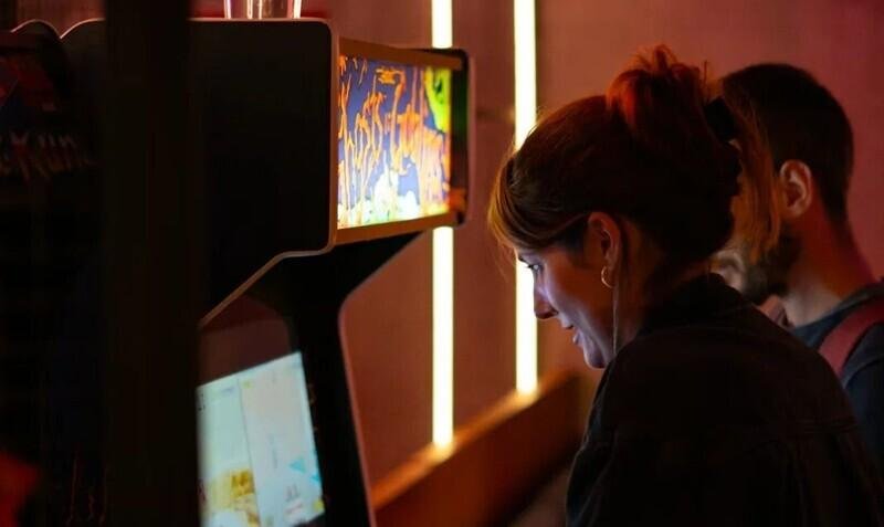 Henkilö pelaa videopeliä arkadipelikoneessa valaistussa ympäristössä